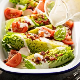 Wedge salad with baby lettuce, cherry tomatoes, bacon and ranch dressing pouring over