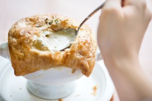 Personal perspective of a girl holding a spoonful of savoury filling from a pot pie with puff pastry crust in a restaurant.