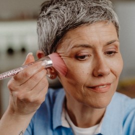 A mature woman applies PÜR Beauty 4-in-1 Powder Foundation, which customers rave gives the 'my skin but better' effect