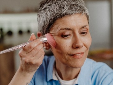 A mature woman applies PÜR Beauty 4-in-1 Powder Foundation, which customers rave gives the 'my skin but better' effect