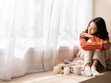 Sad lonely woman with coffee and candle cozy bed with book and blanket. Warm woolen sweater in cold autumn or winter weekend, warm drink.