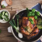 Homemade roasted chicken with green vegetables salad and fresh herbs on rural wooden table viewed from above