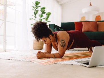 Woman doing plank workout and following workout video on laptop at home