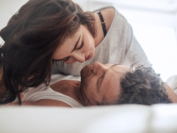 Young couple caressing lying in bed together. Couple in a relationship kissing and cuddling.