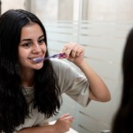 Teen brunette with braces brushing her teeth in front of the mirror